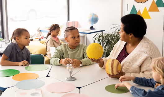 Enseignante montrant un modèle solaire à des enfants assis à une table en classe.