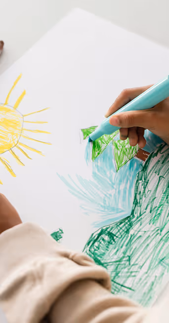 Main dessinant des feuilles vertes avec un marqueur bleu, soleil jaune partiellement visible.