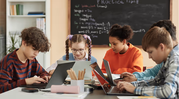 Quatre élèves d’âges différents utilisent des ordinateurs portables à une table en classe.