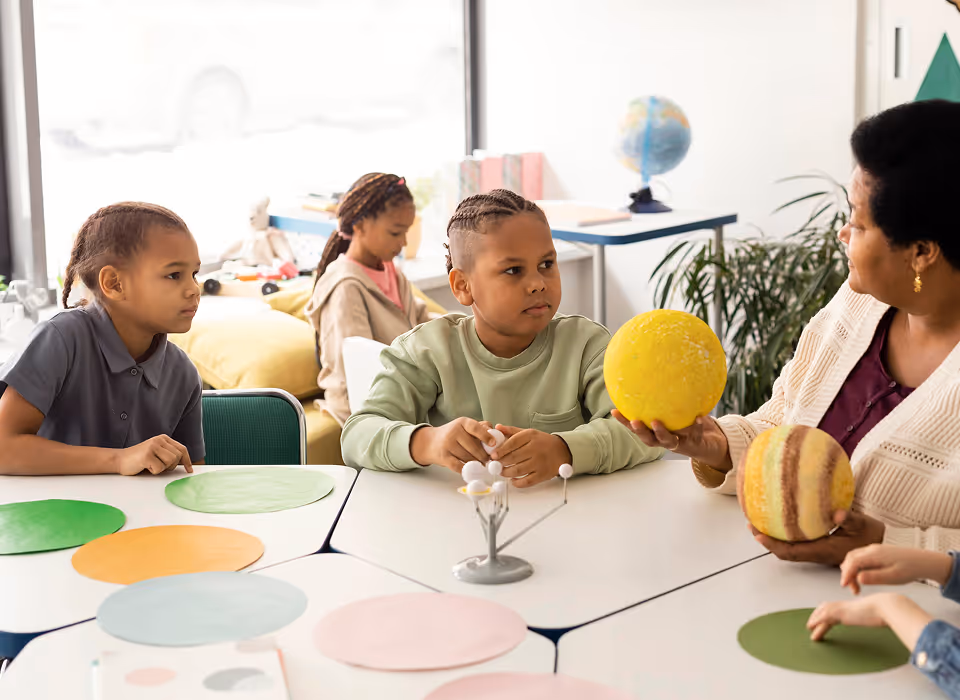 Enseignante montre un modèle planétaire jaune à un garçon pendant qu'une fille les observe en classe.