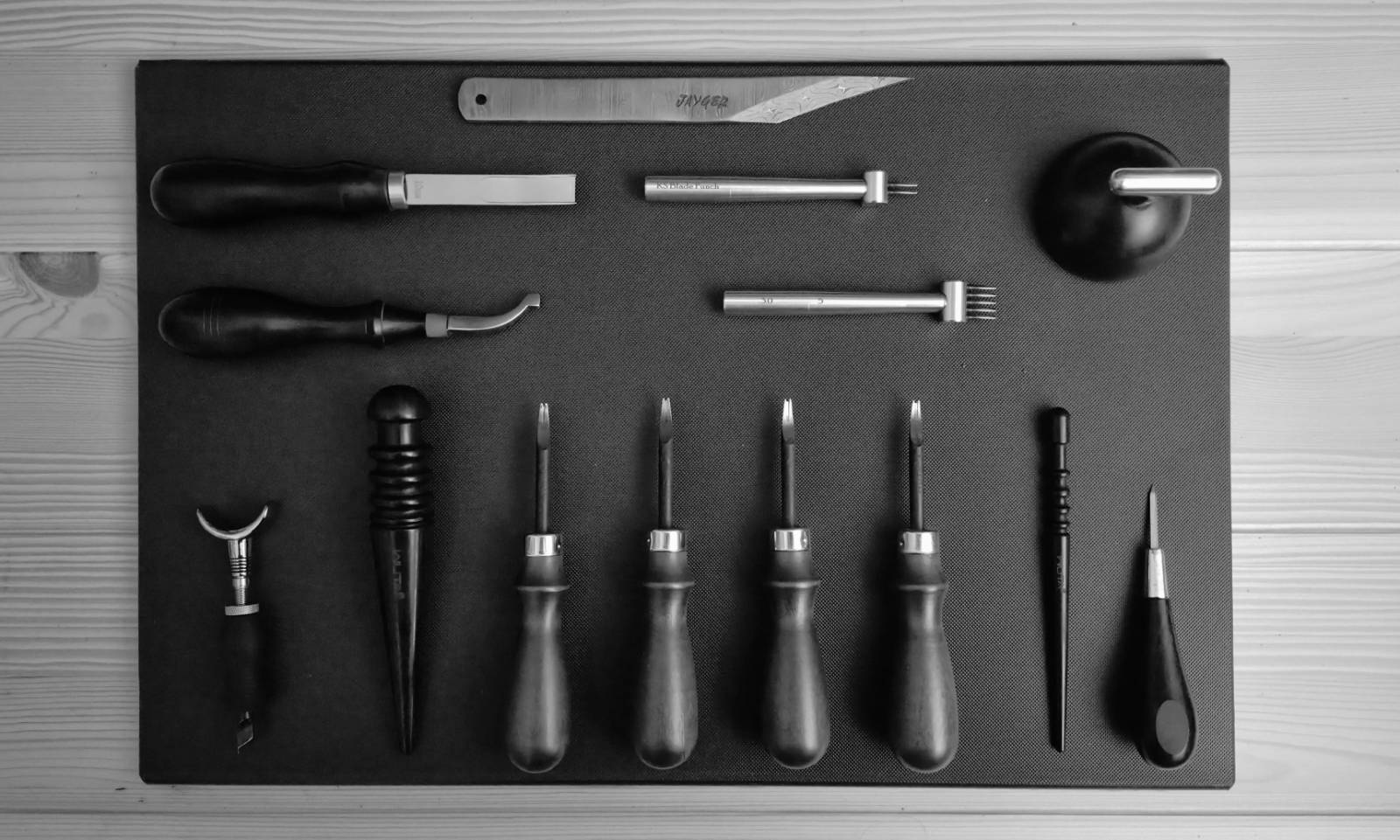 Flatlay black & white photo of leathercraft tools and board on wooden table