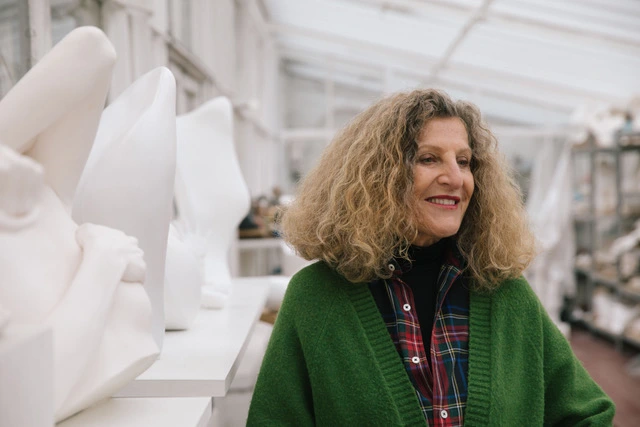 Nicole Farhi with curly hair wearing green cardigan in a bright art studio with white sculptures.