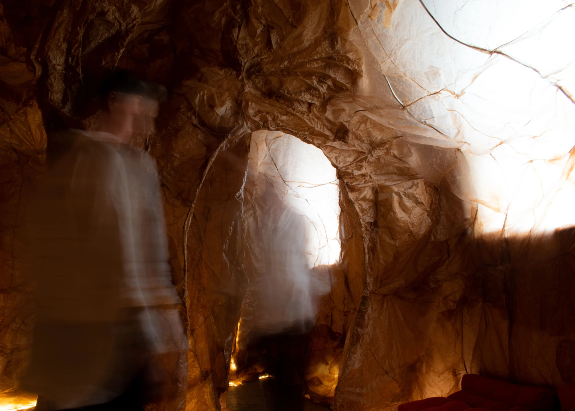 Blurred figures walk through a dimly-lit tunnel with brown textured walls.