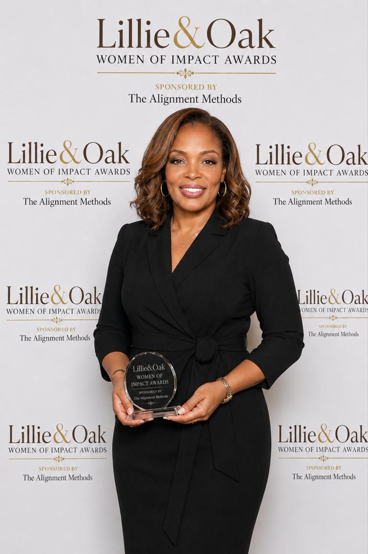 Woman in black dress holding a Lillie & Oak Women of Impact Awards plaque, standing in front of a branded backdrop.