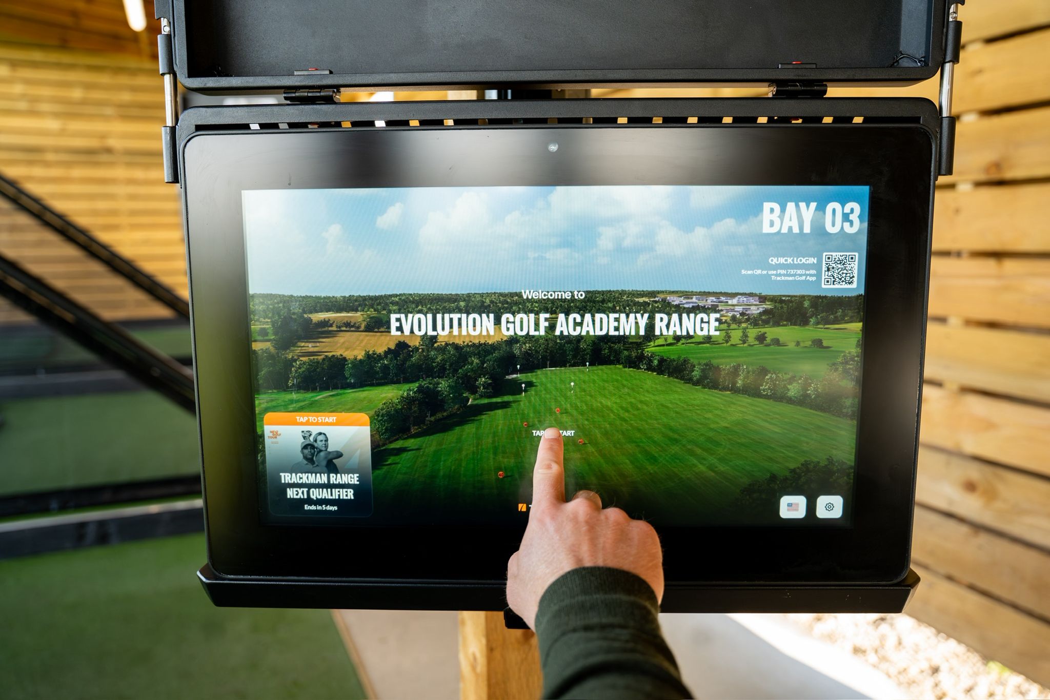 Golfer tapping the Bay 03 TrackMan range screen to start a session at Evolution Golf Academy, Derby