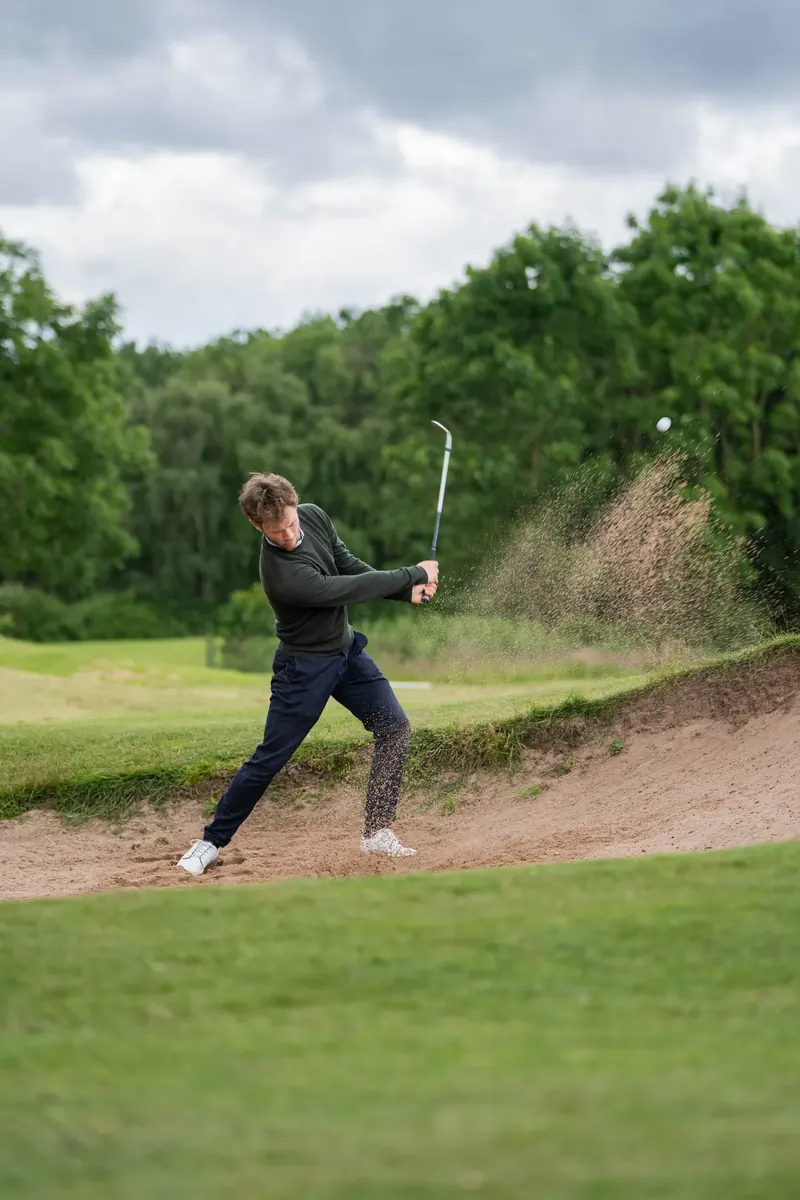 Player practising a bunker shot during a short game golf lesson in Derbyshire.