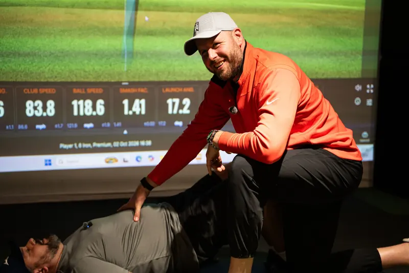 TPI golf mobility session: smiling coach kneeling beside a student lying on the mat at Evolution Golf Academy, Derby.