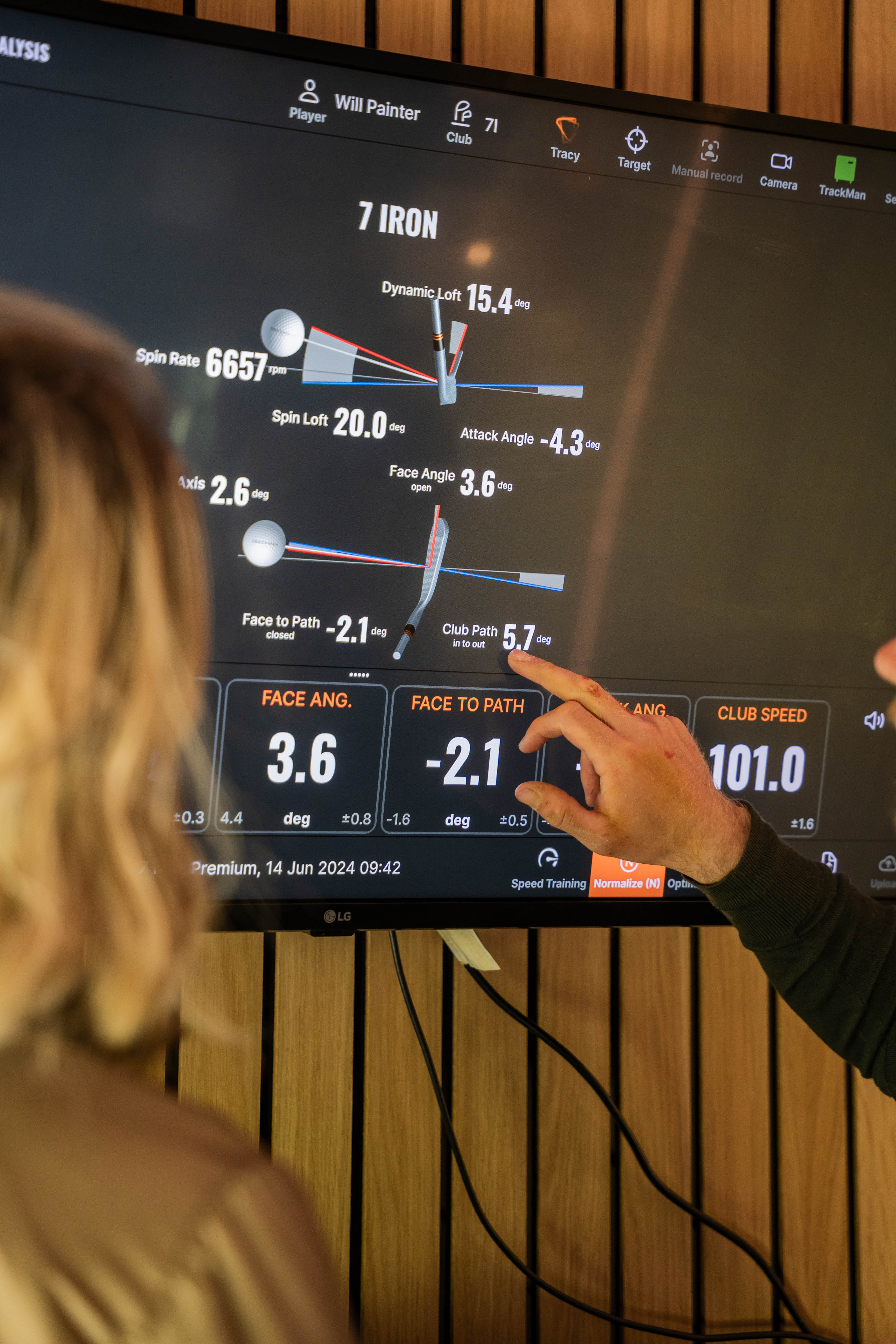 Will Painter pointing at 7 iron club path data on the TrackMan screen while a golfer watches, during a lesson in Derby