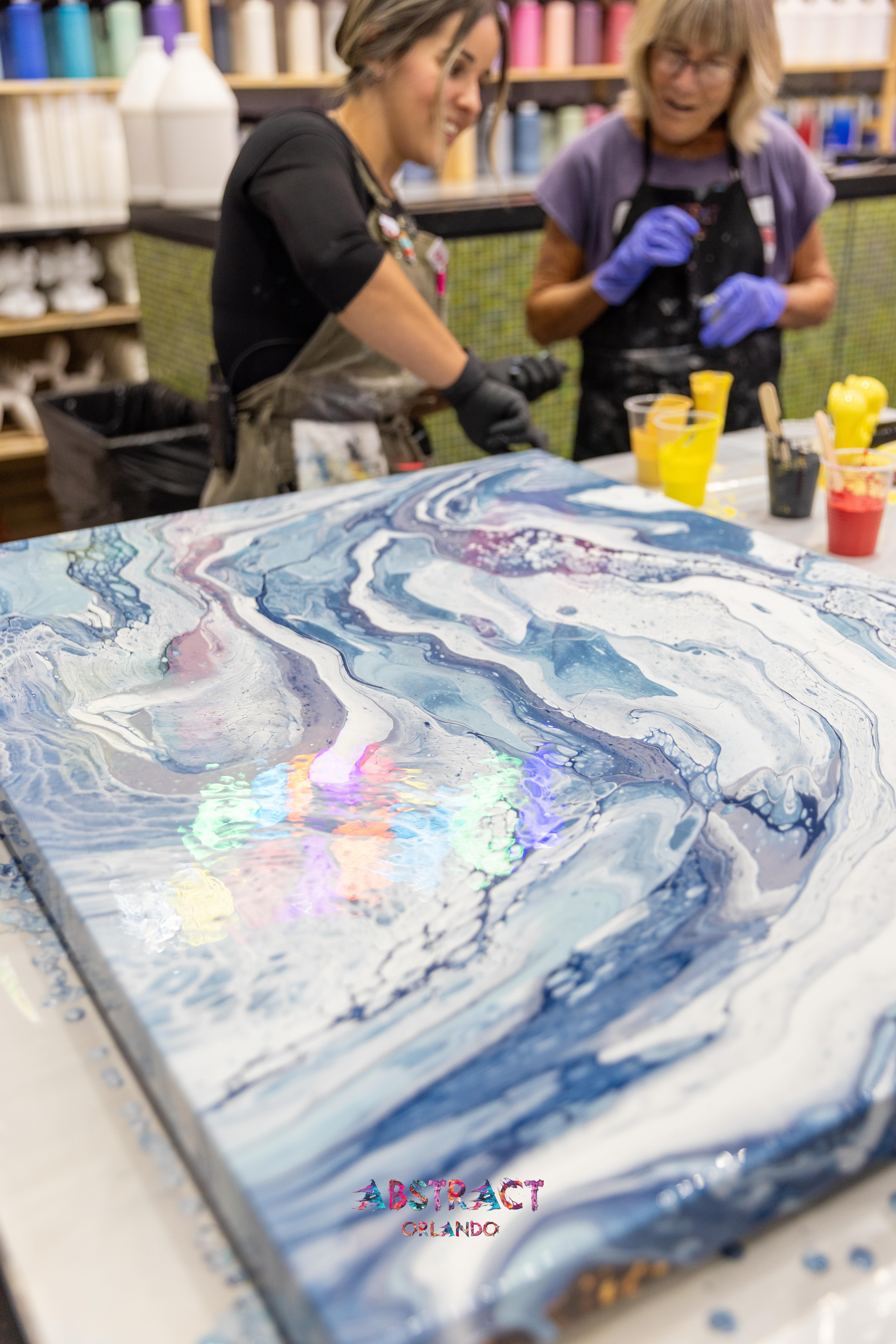 Two guests working together on a large blue fluid art canvas