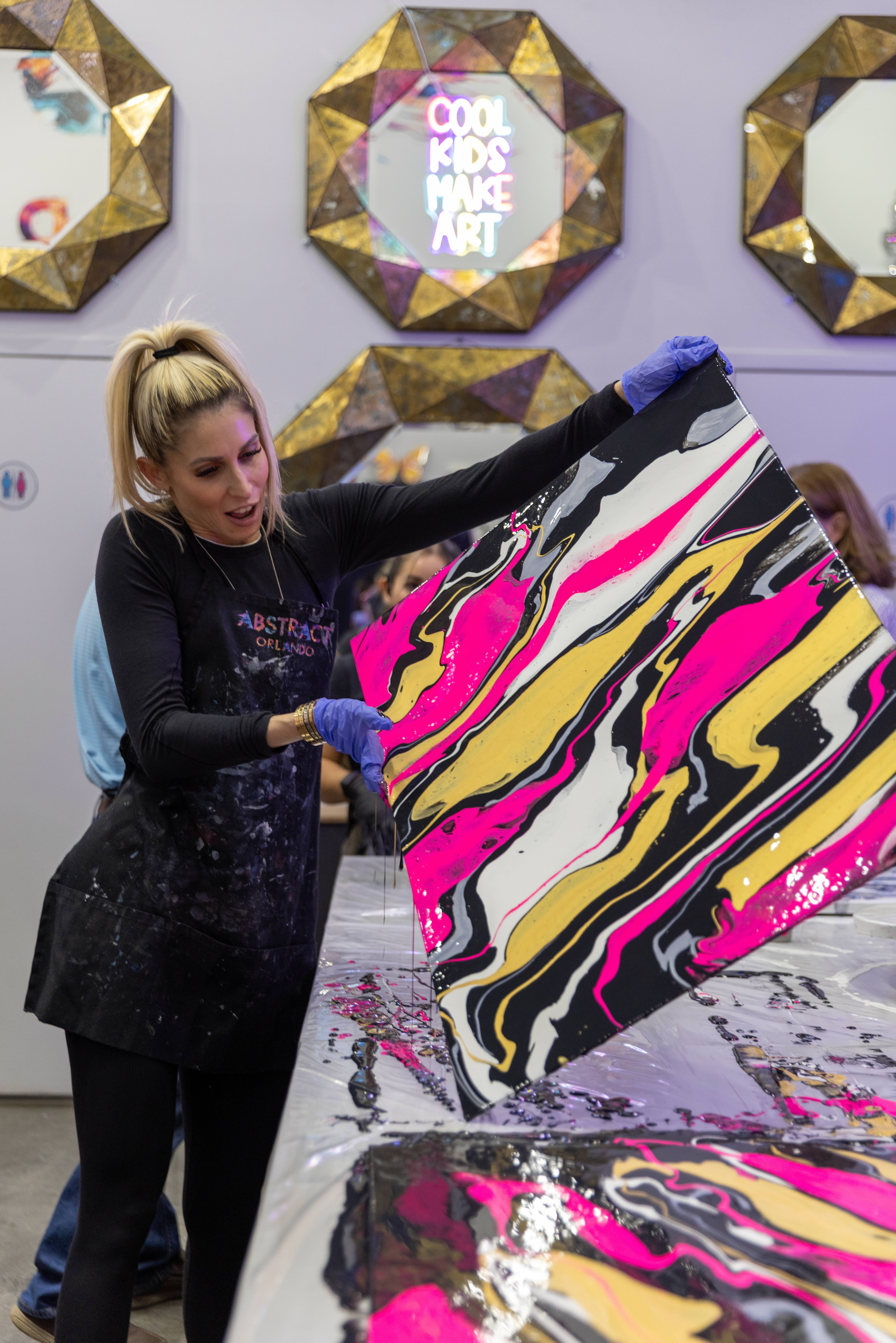 Guest holding up her finished pink, yellow, and black marbled canvas