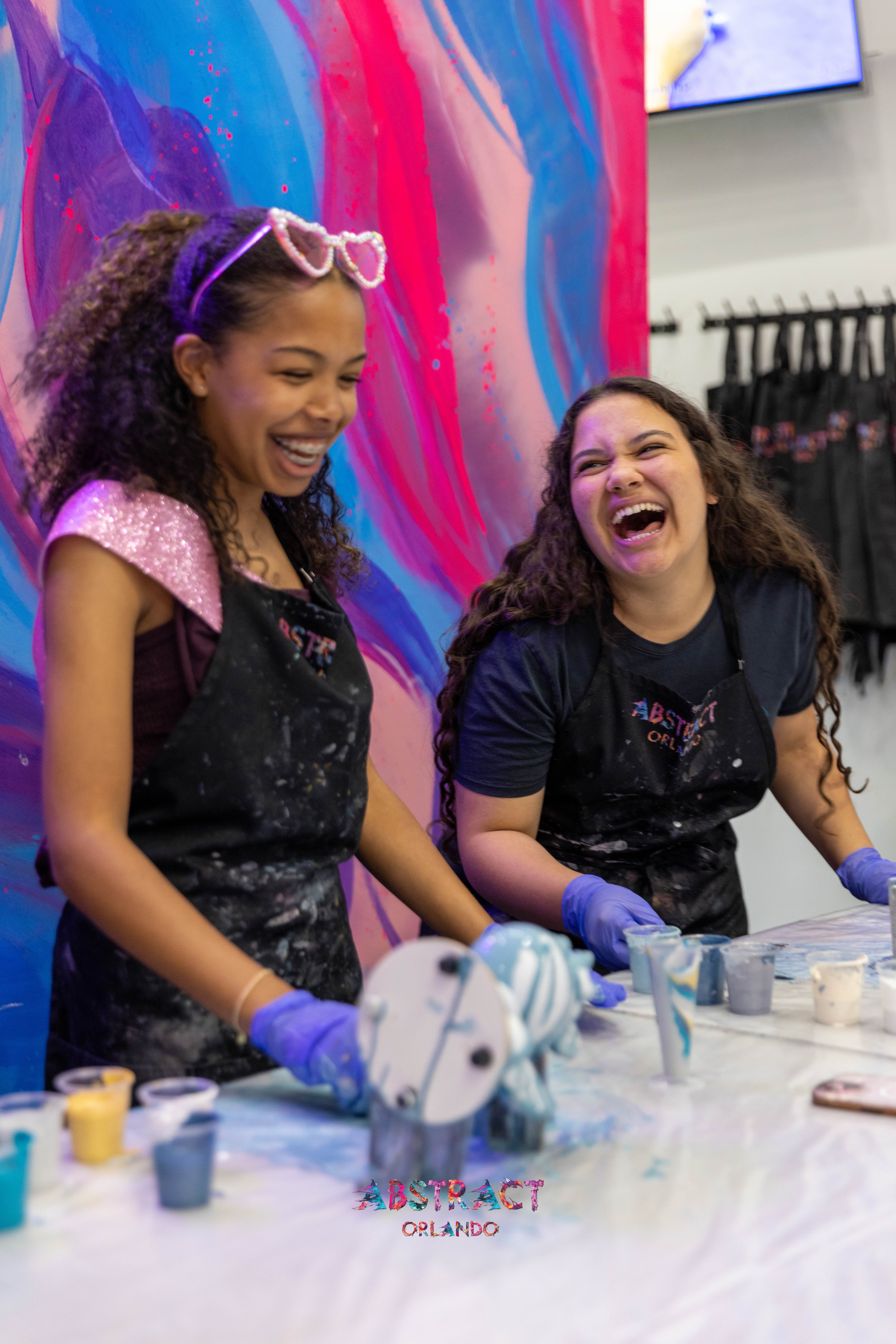Two friends laughing together at their painting station
