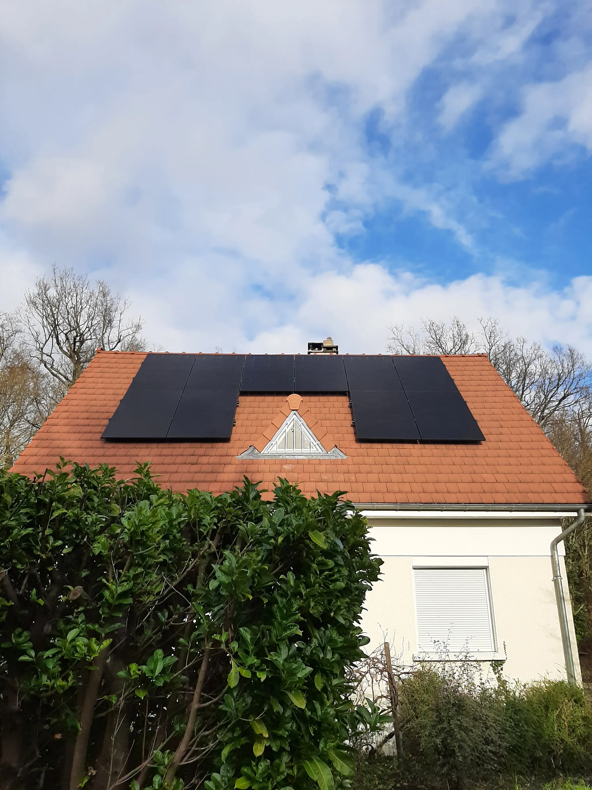 La maison vue du jardin, les modules disposés autour de la chatière sur la toiture en tuiles, à Boissettes (77350)