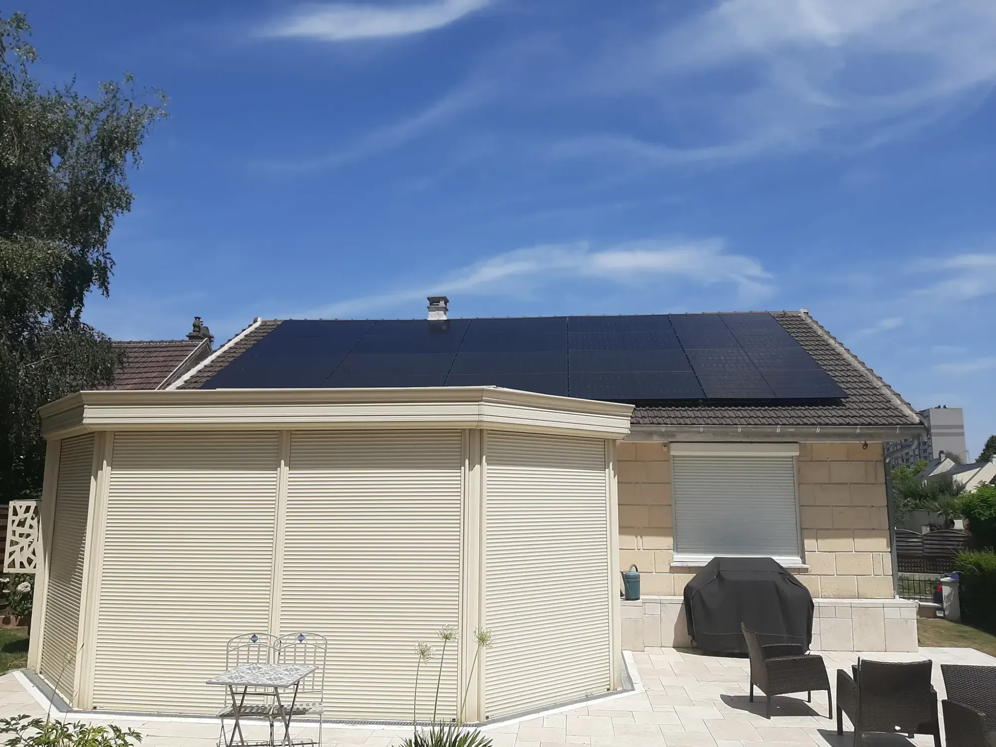 La maison vue du jardin, les modules photovoltaïques noirs sur la toiture en tuiles mécaniques, à Longjumeau (91)