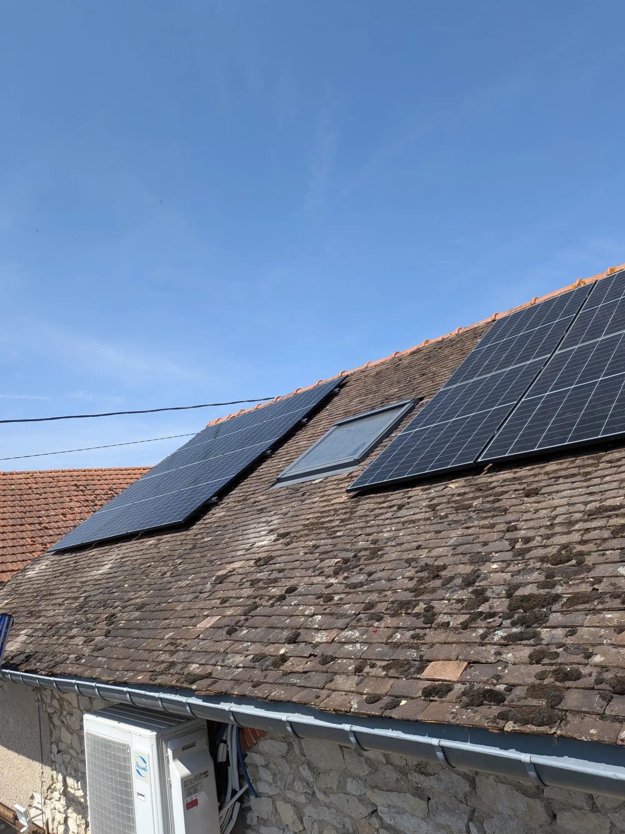 Modules photovoltaïques posés de part et d'autre d'une fenêtre de toit, sur les tuiles plates anciennes, à Pannes (45)