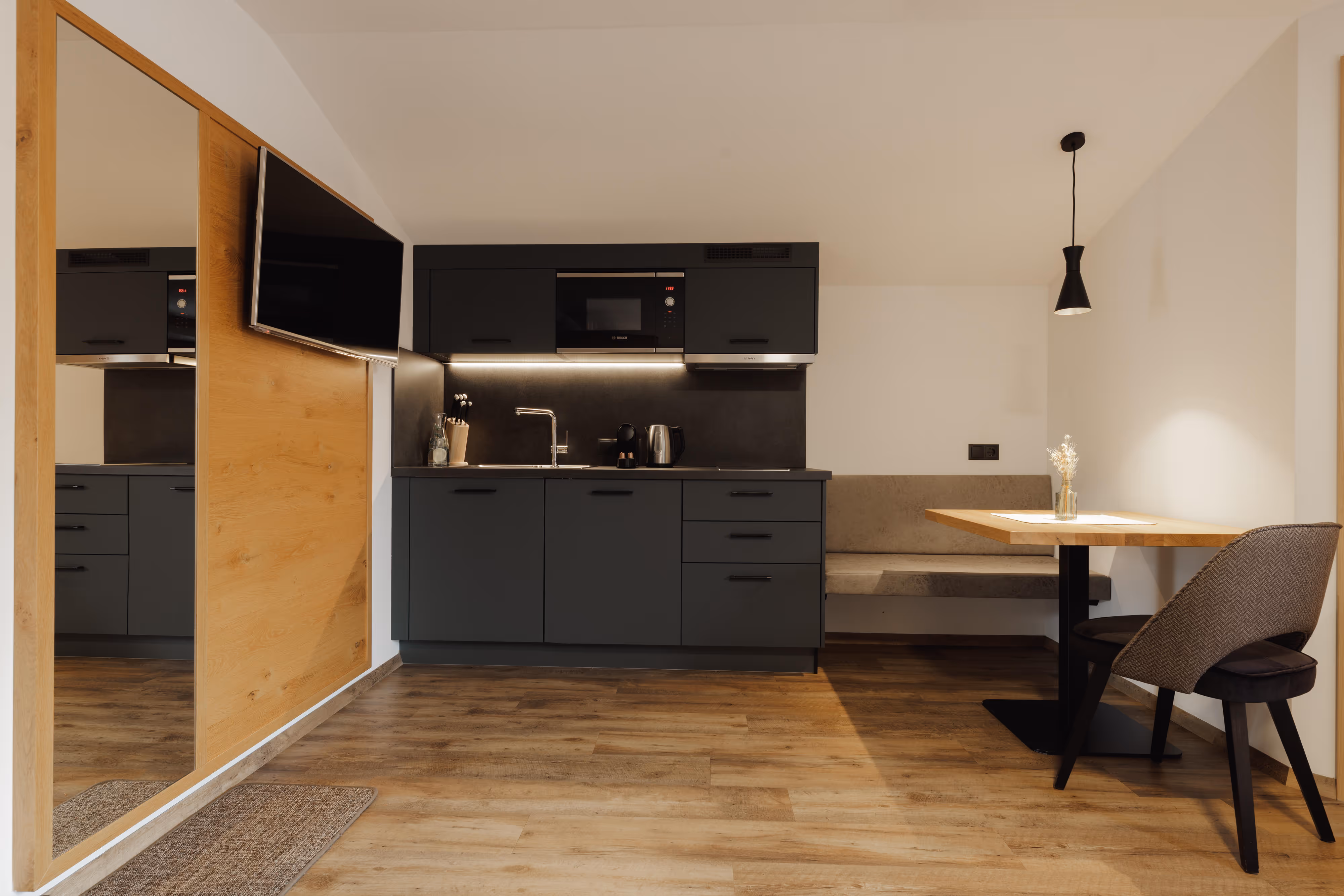 Moderne Küche mit dunklen Schränken, Sitzbank, Holztisch, Stuhl und großem Spiegel an der Wand.
