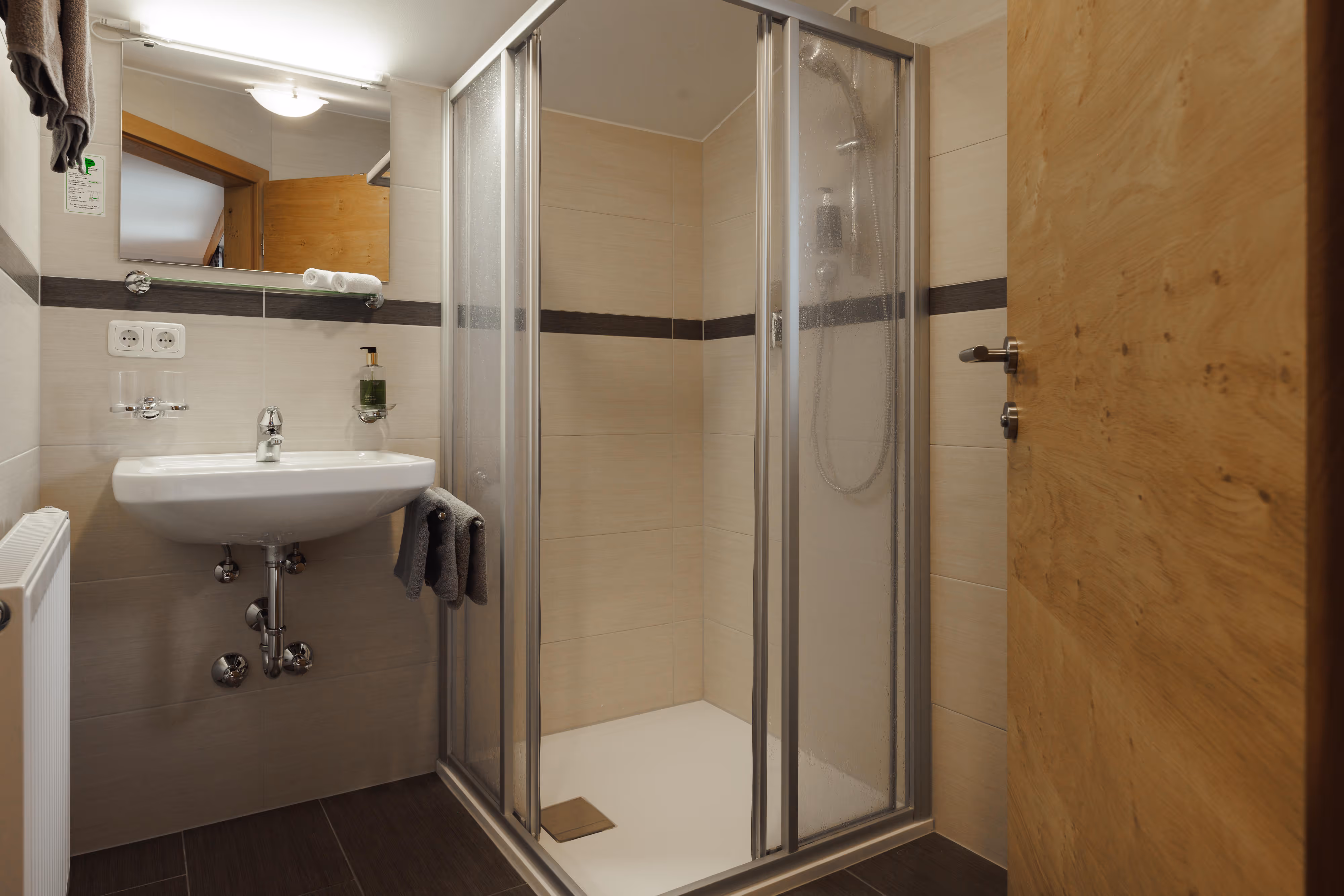 Modernes Badezimmer mit Waschbecken, Spiegel, Duschkabine und Holztür.
