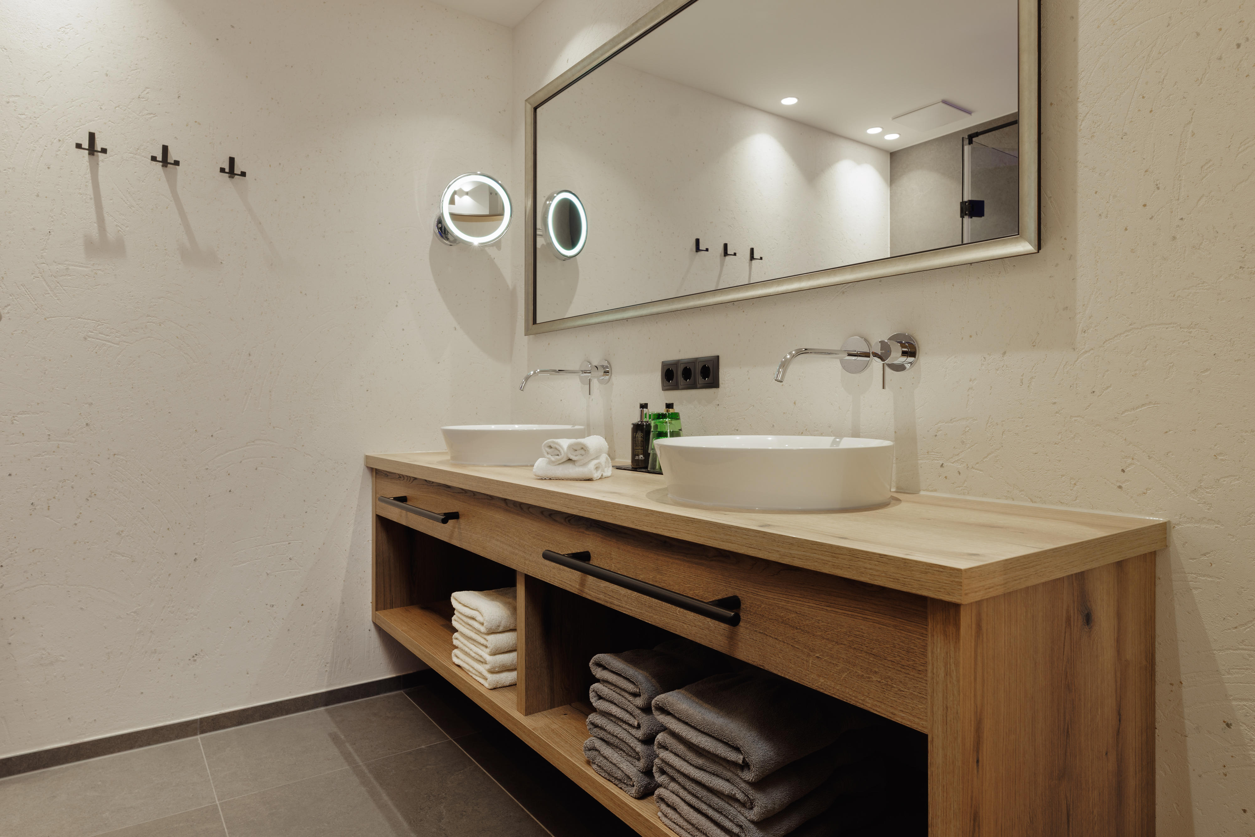 Modernes Badezimmer mit Zwei Waschbecken, großem Spiegel und Holzunterschrank mit Handtüchern.