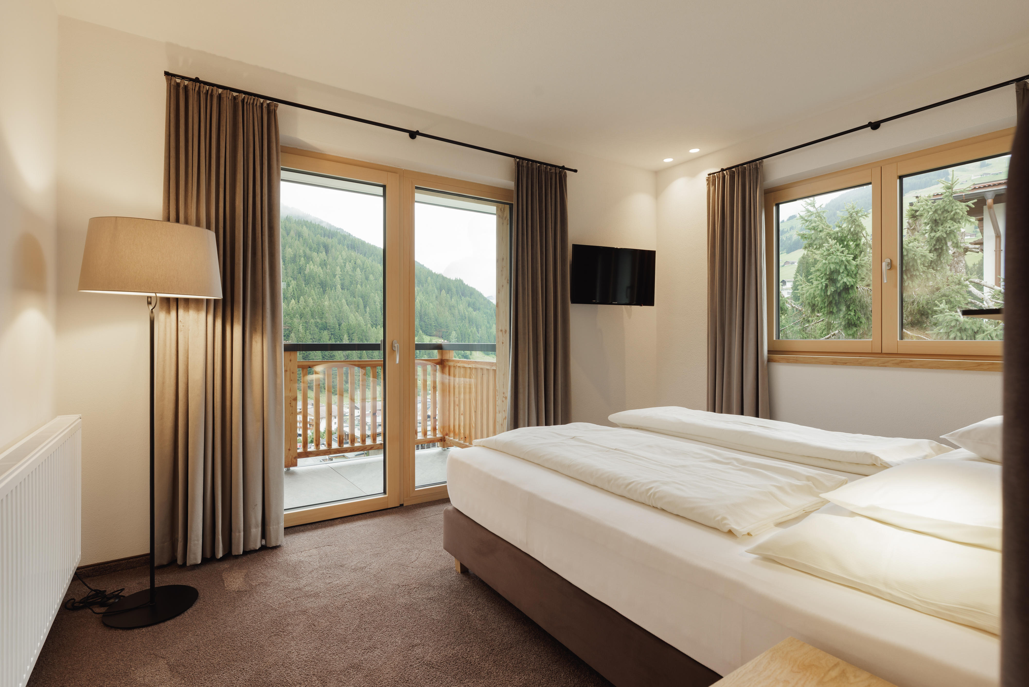Gemütliches Doppelzimmer mit Balkon, großem Bett, TV und Blick auf bewaldete Berglandschaft.