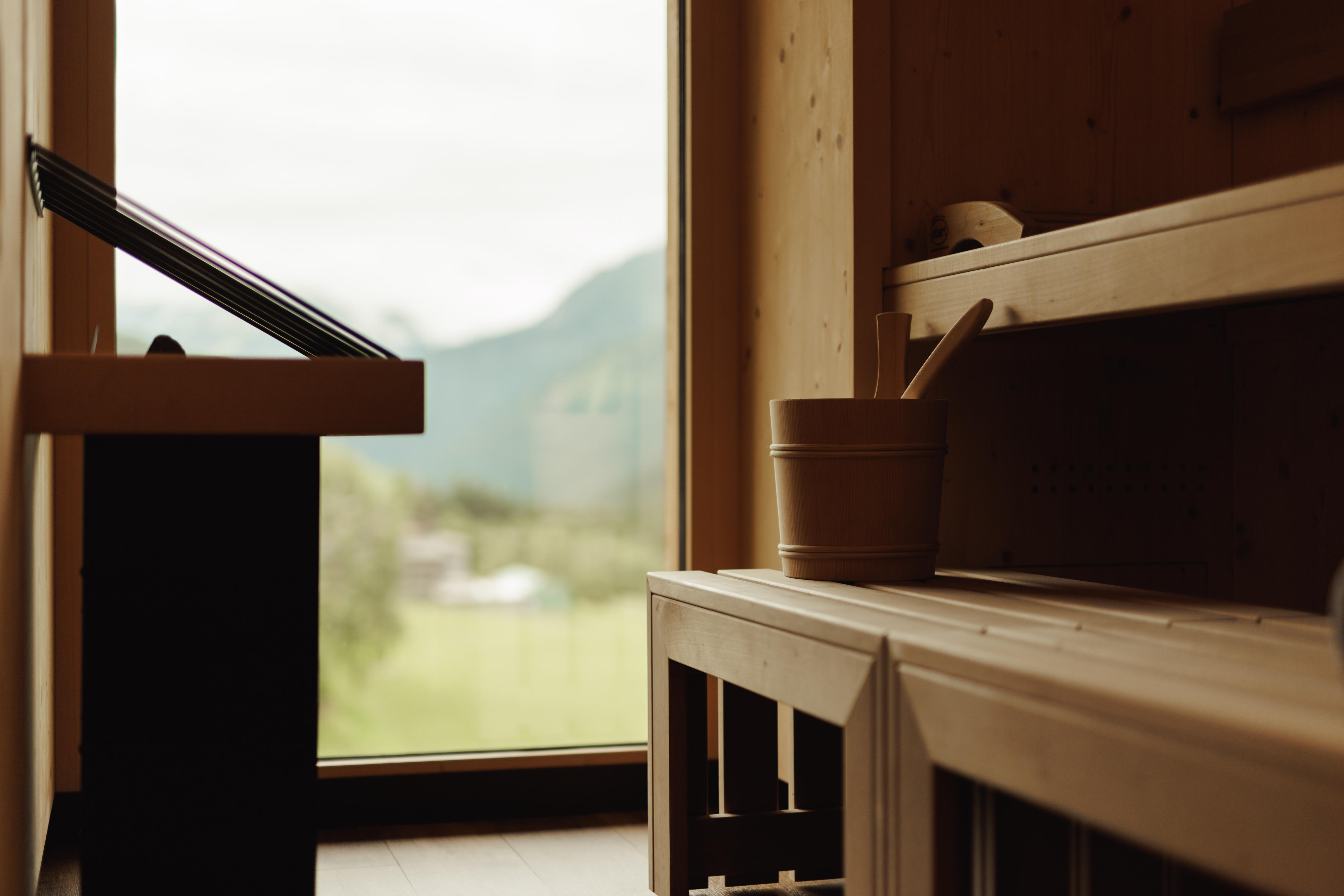 Holzsauna mit Holzbänken und Holzeimer vor großem Fenster mit Bergblick.