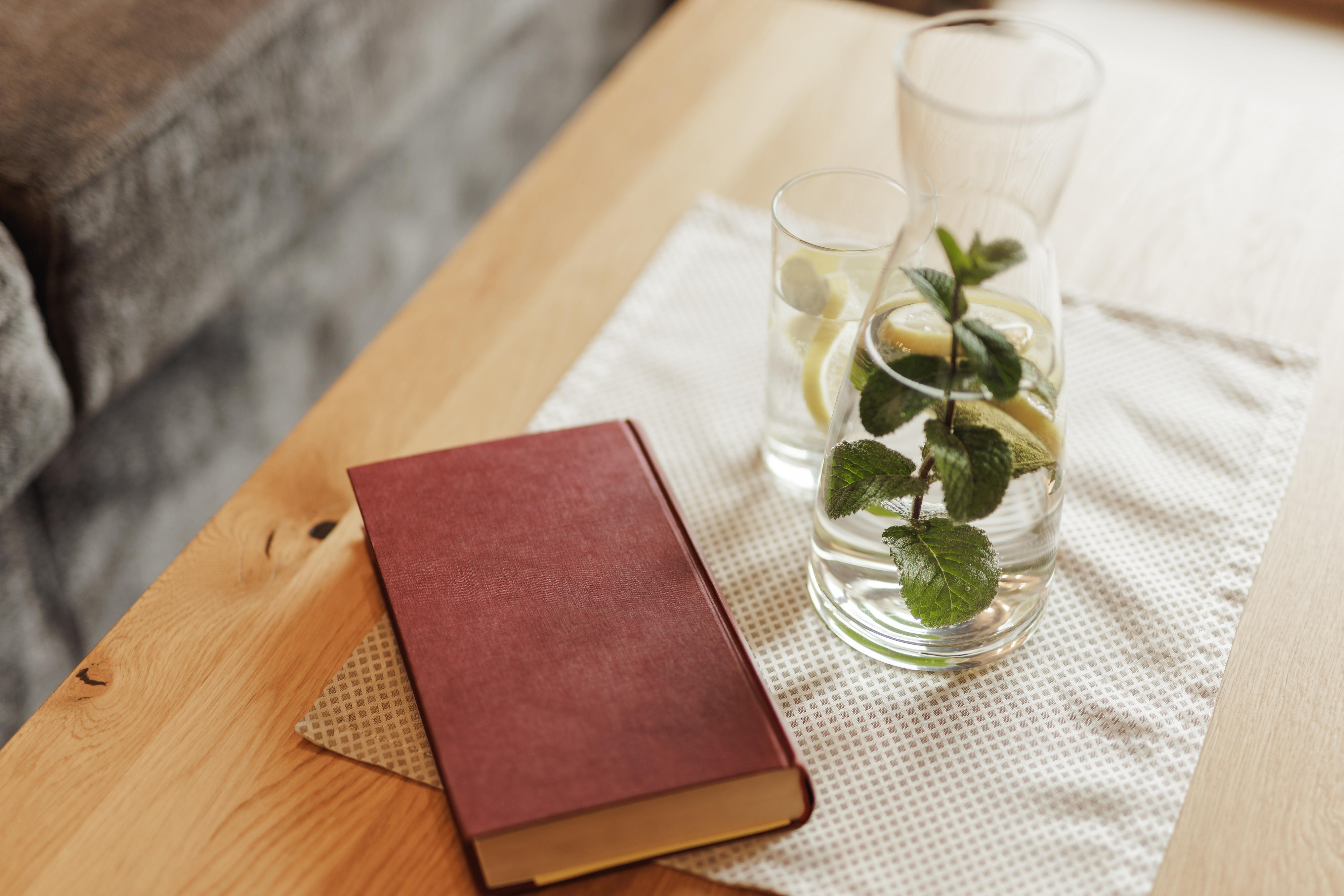 Holztisch mit einem roten Buch, einer Karaffe und einem Glas mit Wasser, Zitrone und Minze.