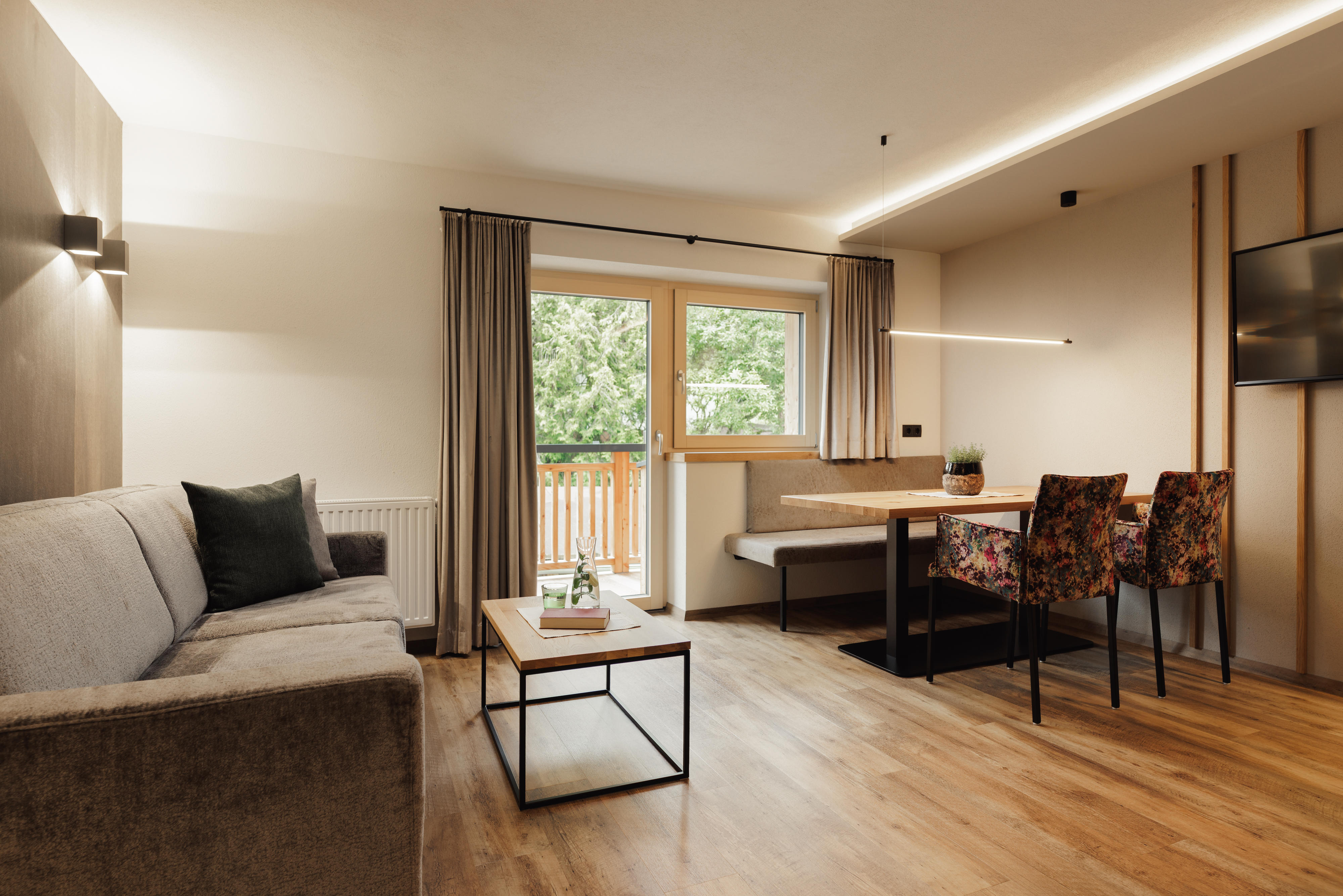 Gemütliches Wohnzimmer mit grauem Sofa, Holztisch, Essbereich und Fernseher an der Wand.