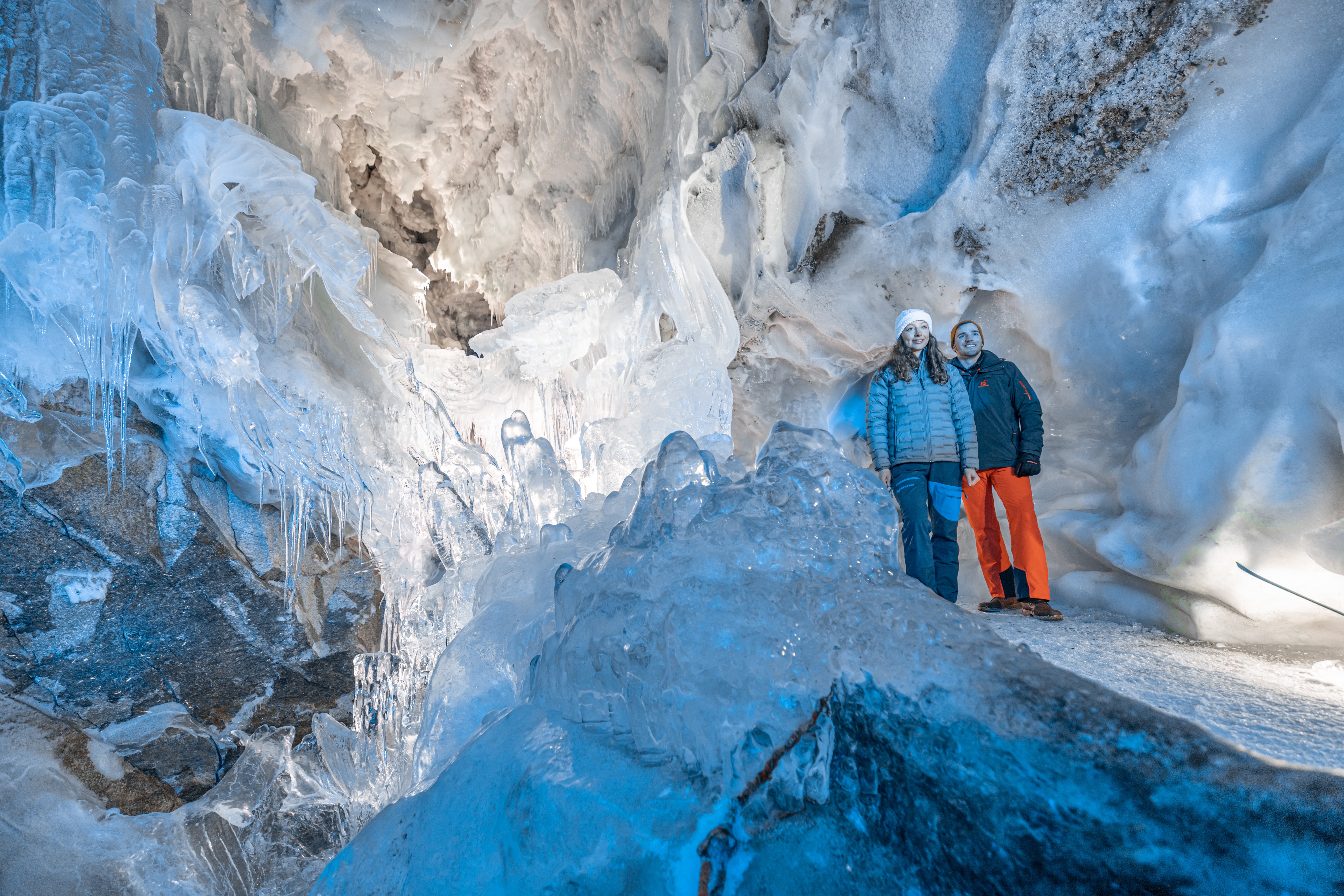 Zwei Personen stehen in einer Eis- und Tropfsteinhöhle mit bläulichem Licht.