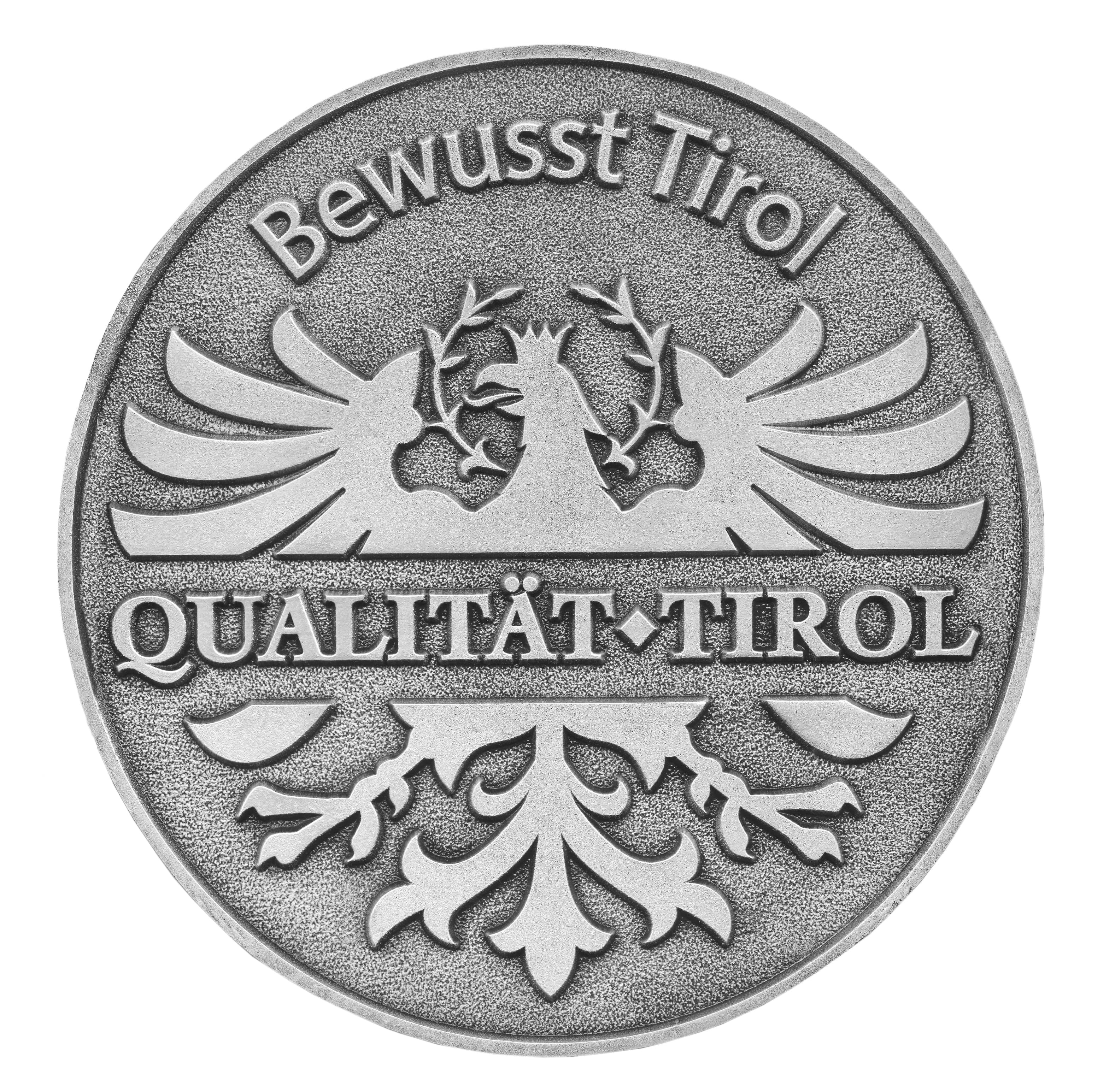 Runde Münze mit Adler und Text Bewusst Tirol Qualität Tirol in Reliefprägung.