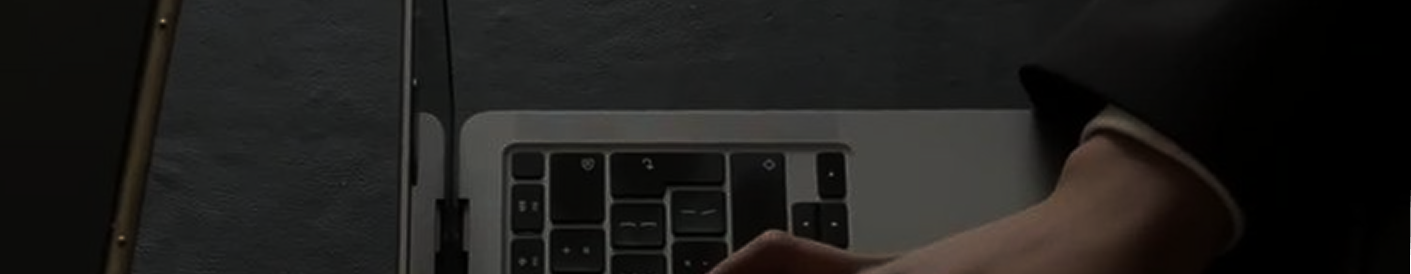 Close-up of a hand typing on a laptop keyboard with a dark background.