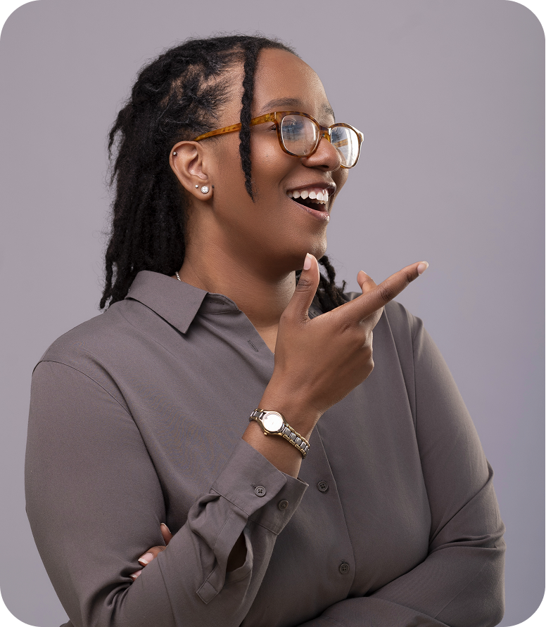 Smiling woman with glasses and dreadlocks pointing to the right against a gray background.