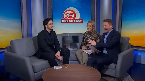 Three people seated on gray couches in a TV studio with a CP24 Breakfast logo on the screen behind them.