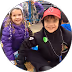 Child and adult smiling together outdoors, both wearing hats and casual clothes.