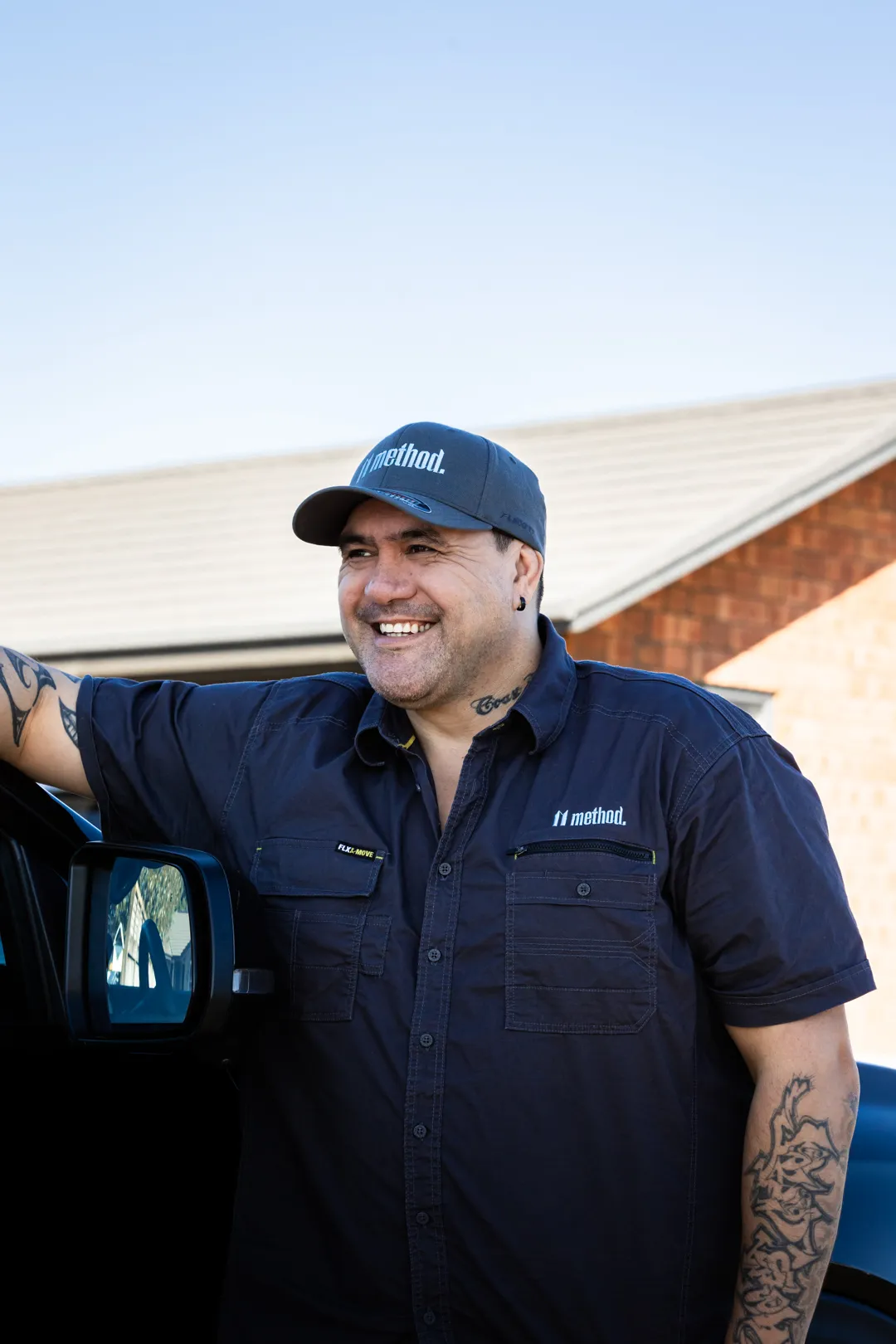 A Method Building Inspections founder, Pita King, standing in front of branded vehicle, wearing uniform and cap, casually, looking into the distance.