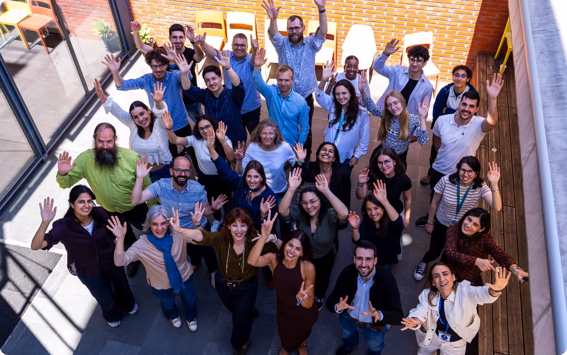 Group of diverse adults standing outside waving and smiling, viewed from above on a patio.