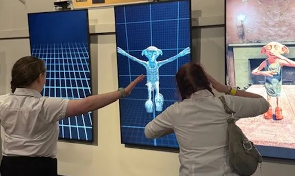 Two people interacting with displays showing a digital figure of Dobby, the house elf from Harry Potter.