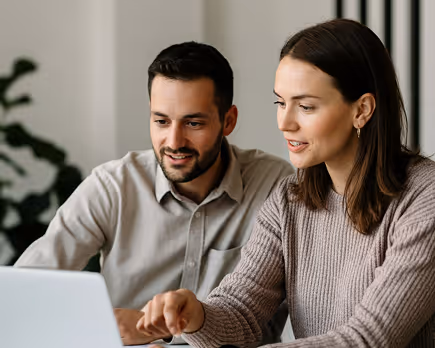 Man and woman looking at laptop screen and discussing together in a casual indoor setting.