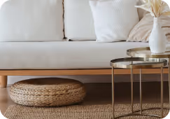 Seating nook with white sofa, round woven cushion underneath, and two round glass-top tables with vases.