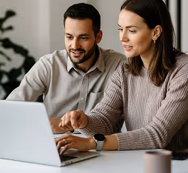 Man and woman sitting at a table discussing and working together on a laptop.