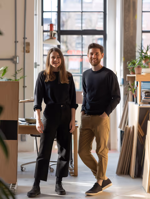 Young man and woman smiling and standing in a bright, modern office space.
