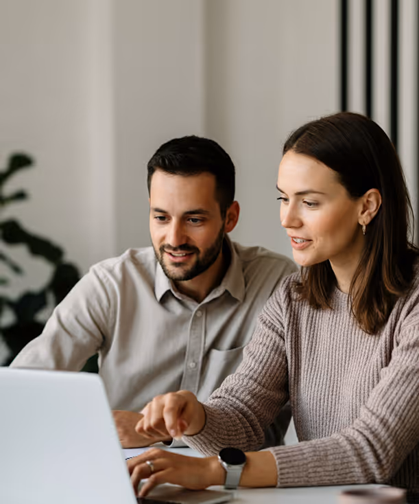 Man and woman sitting side by side, looking at laptop screen, woman pointing at keyboard.