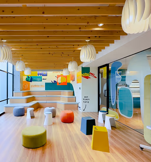 Bright modern room with wooden ceiling beams, colorful stools, tiered seating, and decorative pendant lights.