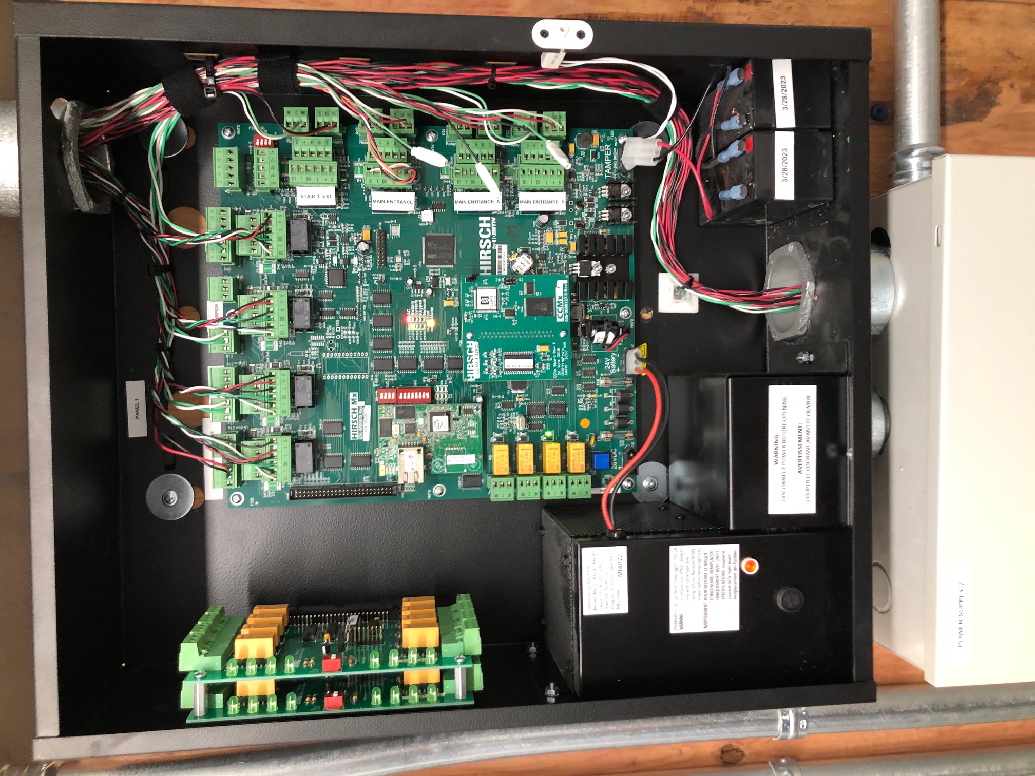 Open electrical panel with Hirsch Access Control circuit board, wiring, batteries, and warning labels inside.