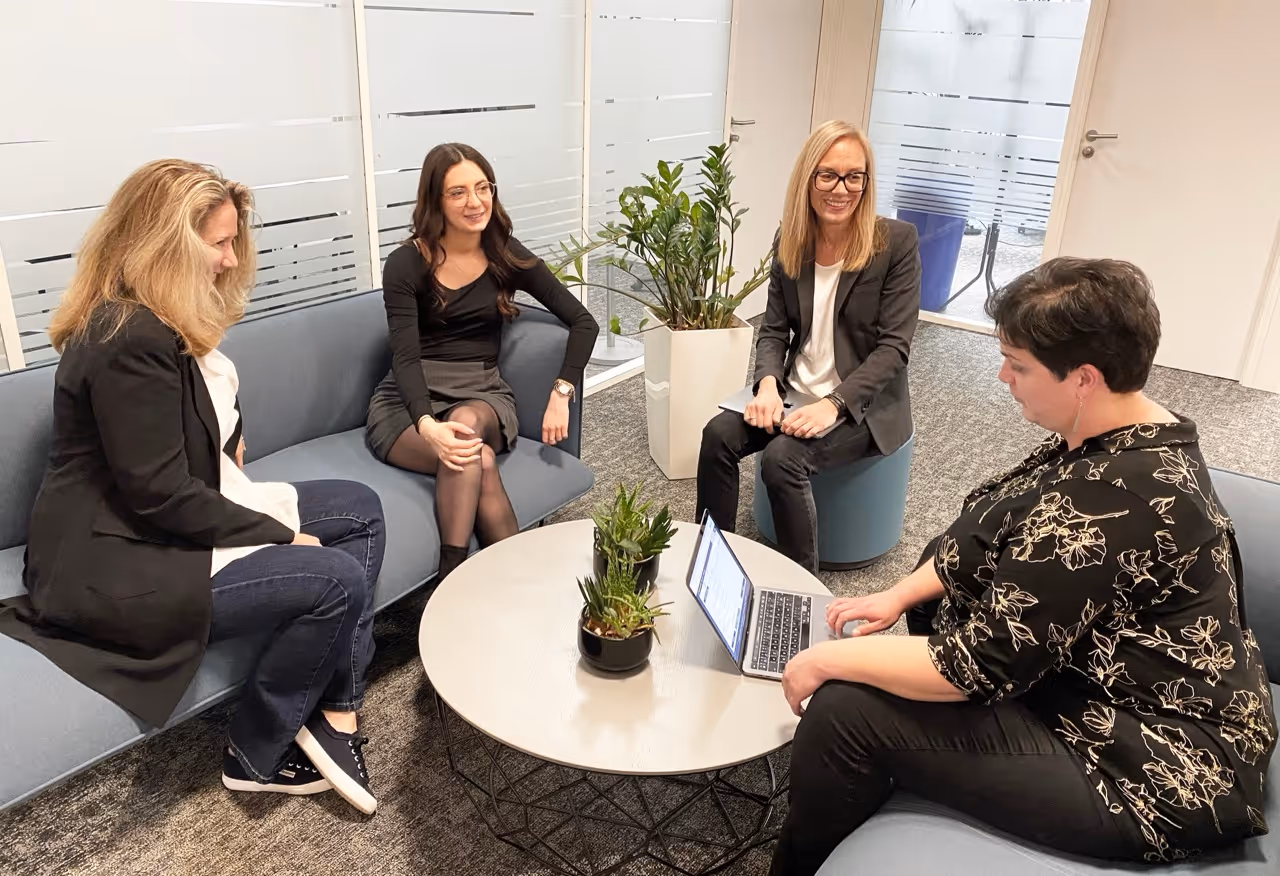Employées de neovoxia assises en discussion dans un bureau moderne autour d'une table basse avec un ordinateur.