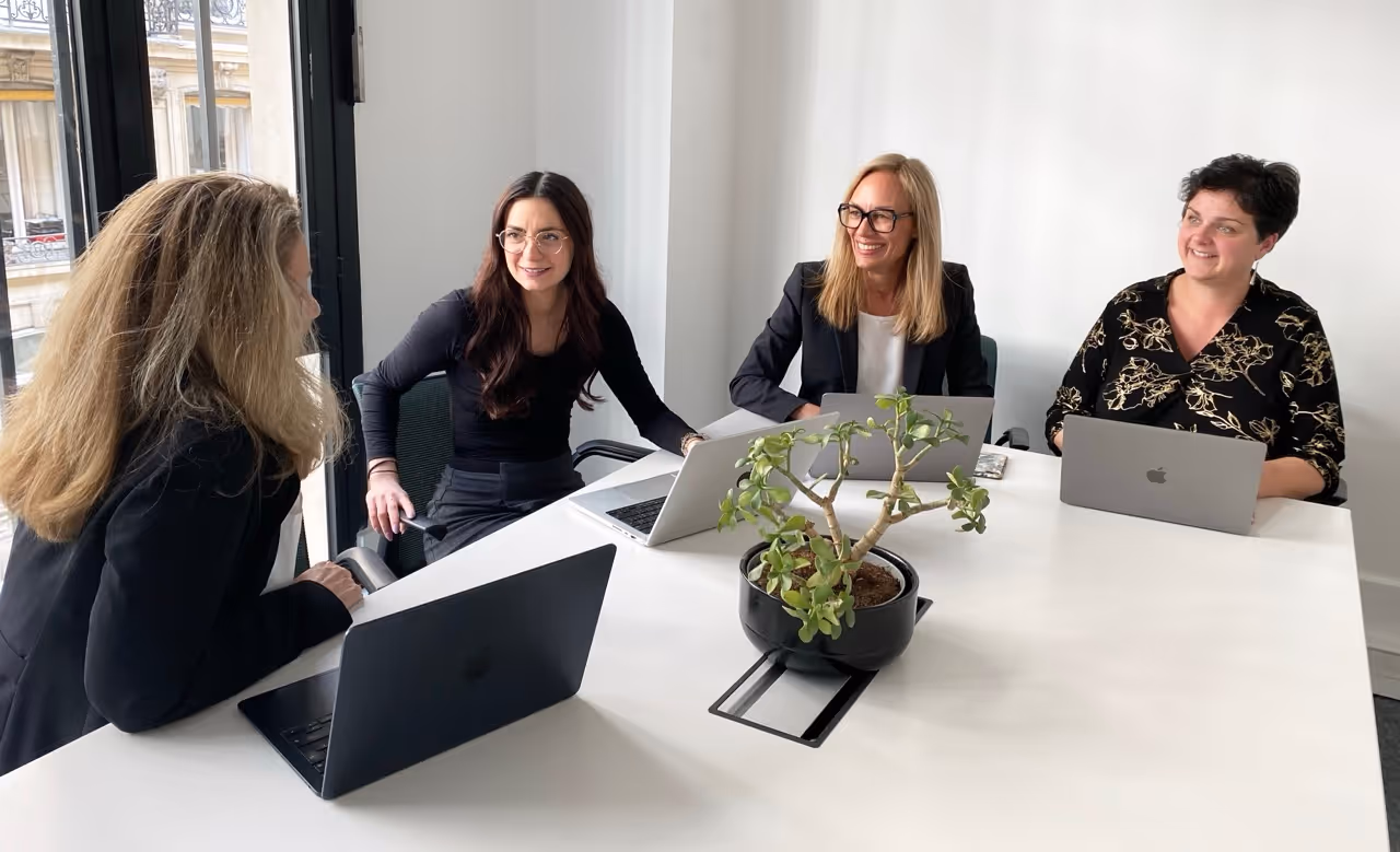 L'équipe Neovoxia avec des ordinateurs portables autour d'une table de réunion blanche avec une plante.