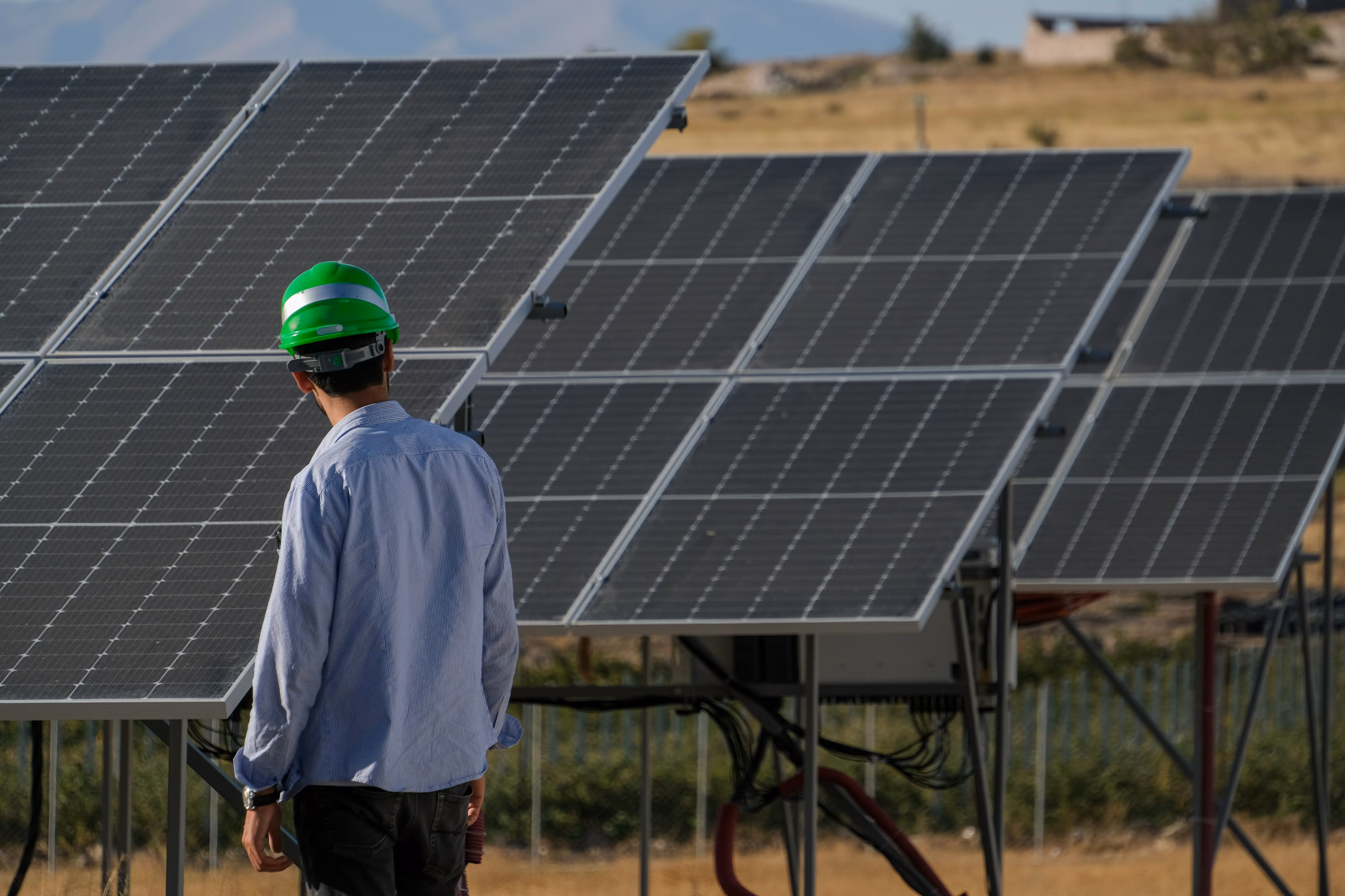 Un homme avec un casque vert inspecte des panneaux solaires dans un champ ensoleillé.