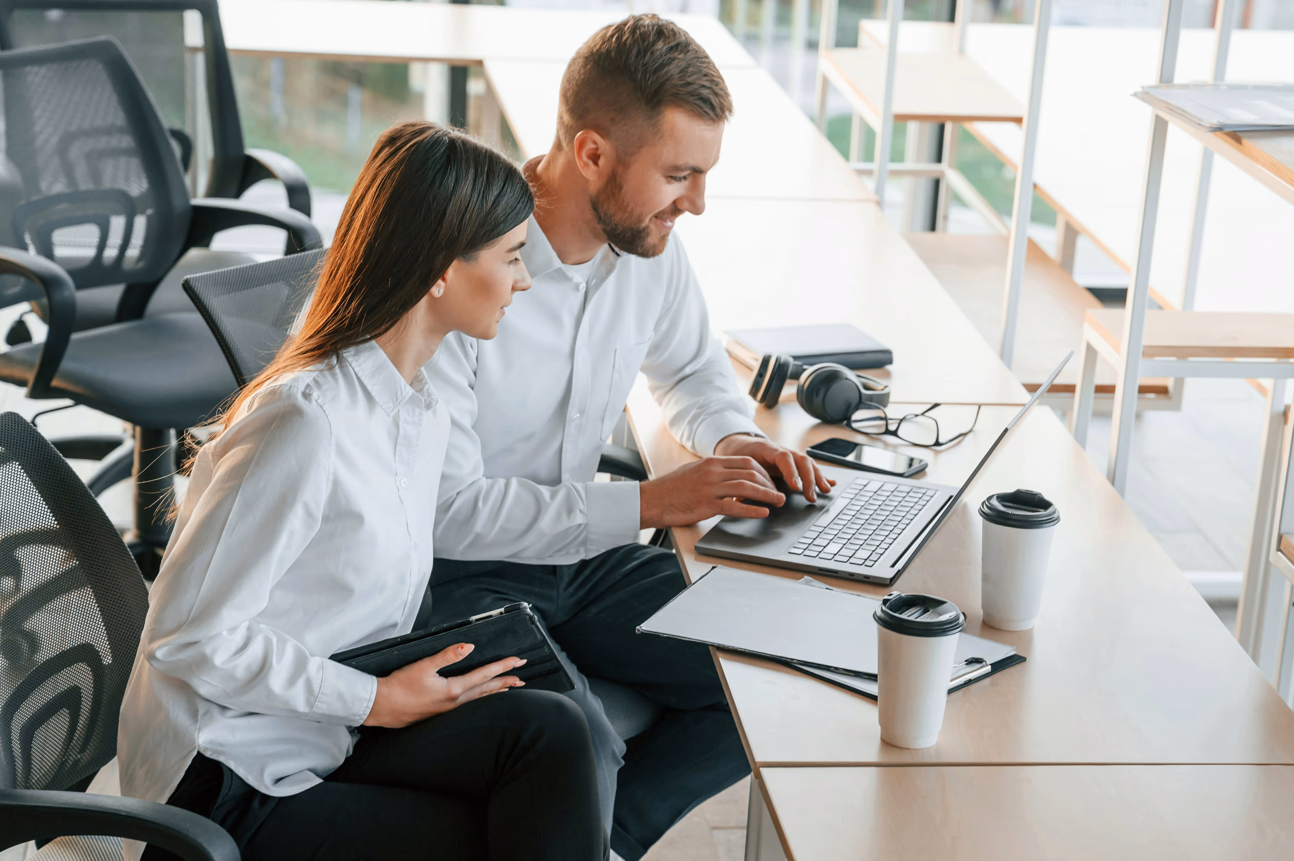 Deux collègues souriants collaborent sur un ordinateur portable dans un bureau moderne.