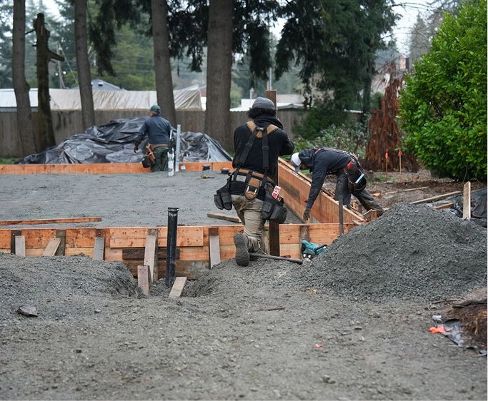 Three construction workers building a concrete foundation framed with wooden boards outdoors.