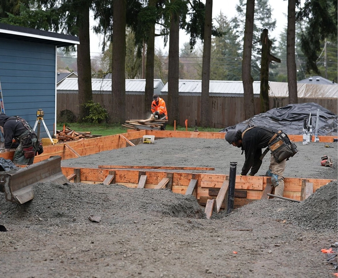 Construction workers preparing and smoothing poured concrete for a house foundation outdoors.