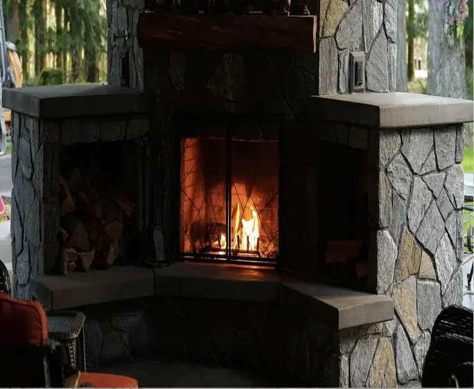 Stone outdoor fireplace with lit fire and wood storage compartments on each side.