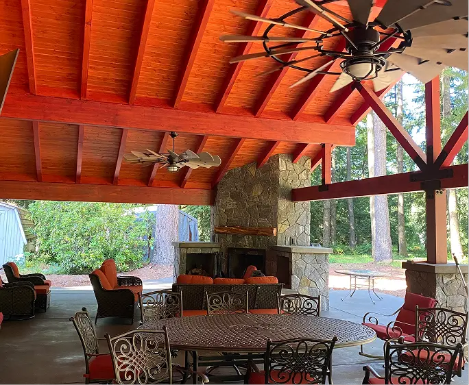 Covered outdoor patio with stone fireplace, ceiling fans, metal table, and cushioned chairs.