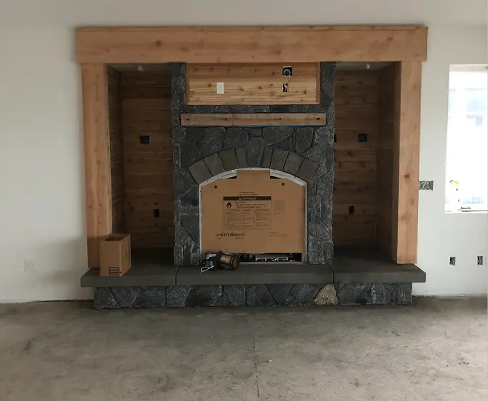 Unfinished room with a stone fireplace framed by wood beams and construction materials on the floor.